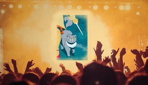 Audience in front of lit stage with partial cover reveal hand holding wand next to grey cat staring upwards