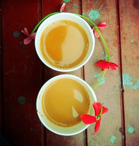 two cups of tea with red flowers on wooden table with green paint spashes