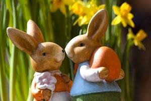 Customs: 2 ceramic Easter bunnies, one holding an orange egg with daffodils in the background