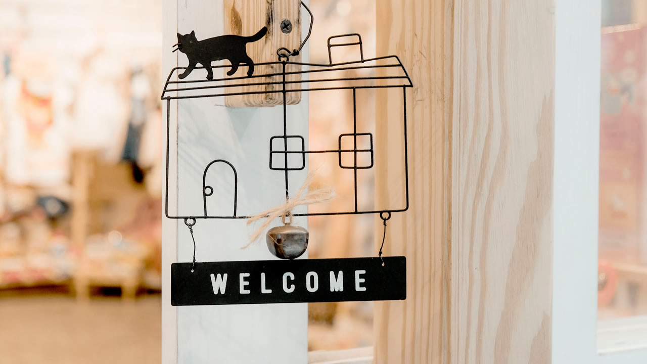 Welcome sign on an open glass door: Black wire house with cat on the roof and Welcome sign below