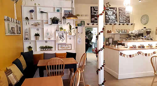 Inside the Twisted Current Cafe. White shelves with nautical artwork, wooden tables, bright interior