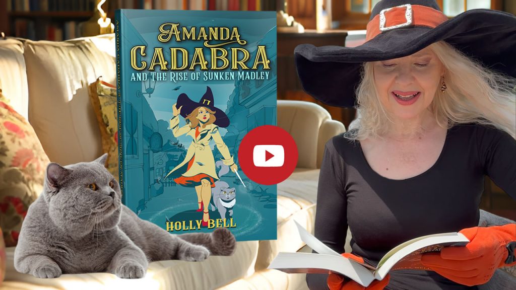 Click to go to video of Holly Bell reading Chapter 1 of Amanda Cadabra and The Rise of Sunken Madley. Image of Holly Bell in witch hat reading from Amanda Cadabra book while grey British Blue cat looks up at her grumpily from the sofa in a sunny room