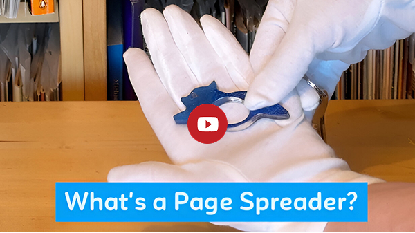 A laser royal blue page spreader in the shape of Tempest The Cat held against a white glove. Text: What's a page spreader?