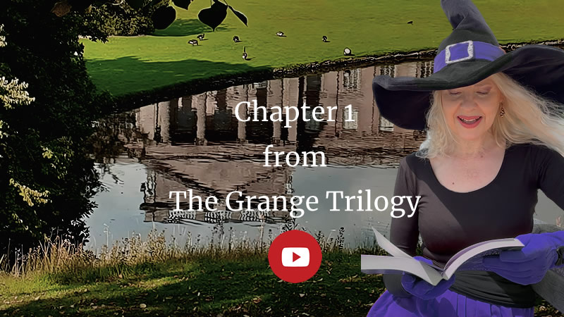 reflection in a lake of a stately home under a tree, grass in the foreground. Eerie late afternoon feeling. Text: Chapter 1 from The Grange Trilogy. Holly Bell wearing black top and witch hat with purple band, gloves and skirt, on the right reading from a book.