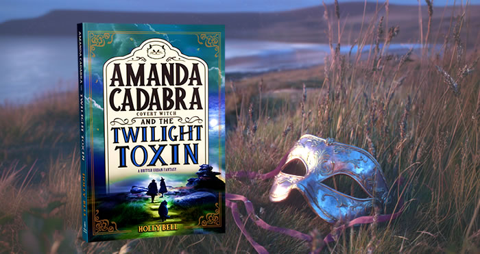 The book Amanda Cadabra and The Twilght Toxin in wild grass beside a Venetian mask, near the shores of a lake at twilight.