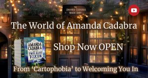 Cosy magical shop, orange light coming from door and window, glwoing in the dark, lights all around. Text: The World of Amanda Cadabra Shop Now OPEN. From 'Cartophobia' to welcoming you in.