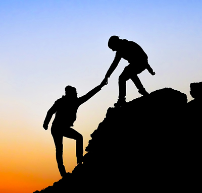 Silhoute of one person helping another to climb up a steelp slope at sunset
